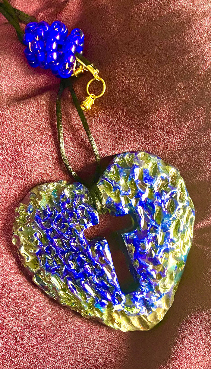 Have A Heart ! Each heart pendant is handmade with love! It is 3"x 3" and weighs approx. 3ozs. This pendant has a royal blue and gold metallic raku glazes that renders a unique translucent patina. The heart has a cut out cross in the center with a textured pattern. It holds a spiral of royal blue mini beads on a spiral copper wire. This pendant has a nice 12" black suede cord!