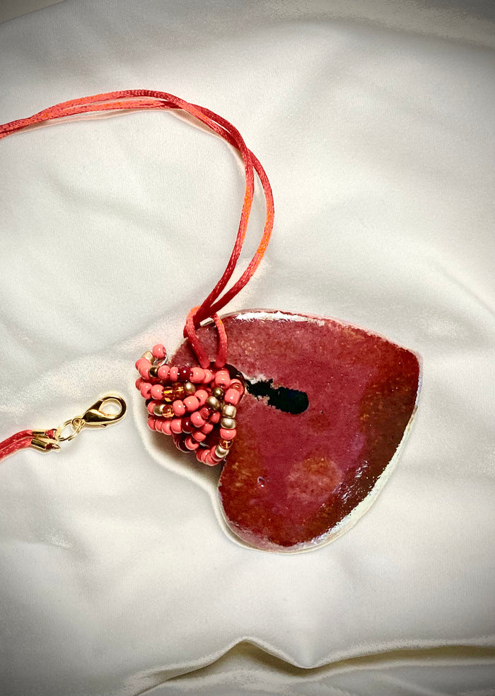 Each heart pendant is handmade with love! It is 3"x 3" and weighs approx. 3ozs. This pendant has a red violet and gold metallic raku glazes that renders a unique translucent patina. The heart has a smooth surface . Both sides are are different and equally beautiful! It holds a spiral of red violet mini beads on a spiral copper wire. This pendant has a nice 12" red suede cord!