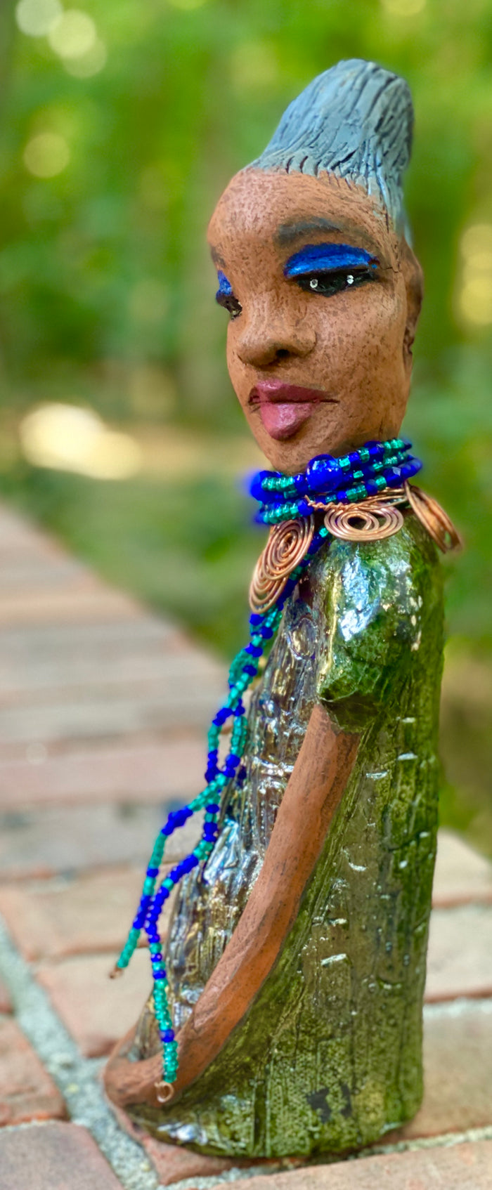 Meet  Emma Again! Emma went and got her a makeover too. She was jealous of Eonna! Emma stands 12.5" x 3. 5" x 4" and weighs 2.04 lbs. She has a lovely honey brown complexion with reddish brown lips. She has a braided clay hairstyle.  Emma has a colorful metallic green antique copper glazed dress. She wears a spiral copper wire necklace on top of a multicolored blue beaded collar. Check out Emma before and after pics. With eyes wide opened,  Emma has hopes of finding  her way into your home!