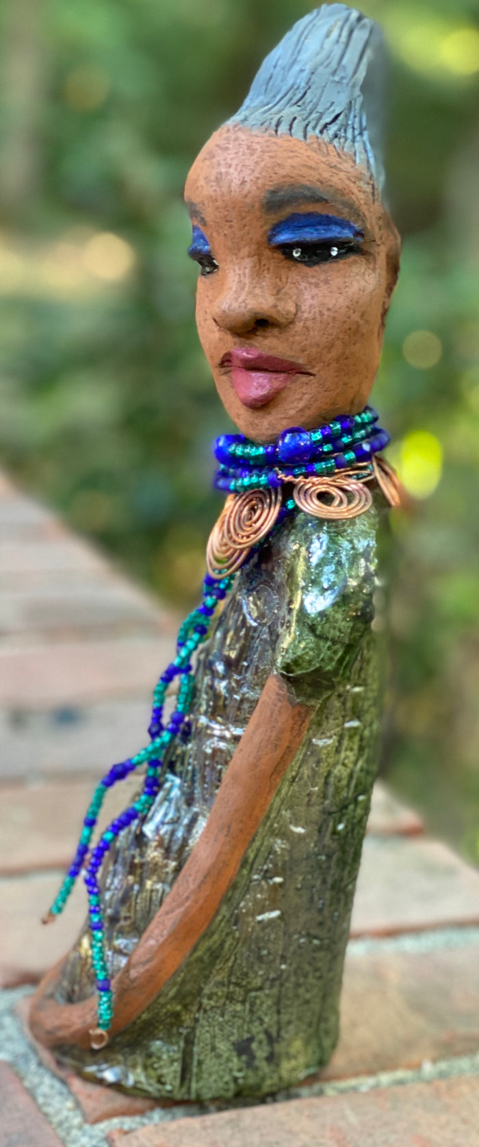Meet  Emma Again! Emma went and got her a makeover too. She was jealous of Eonna! Emma stands 12.5" x 3. 5" x 4" and weighs 2.04 lbs. She has a lovely honey brown complexion with reddish brown lips. She has a braided clay hairstyle.  Emma has a colorful metallic green antique copper glazed dress. She wears a spiral copper wire necklace on top of a multicolored blue beaded collar. Check out Emma before and after pics. With eyes wide opened,  Emma has hopes of finding  her way into your home!