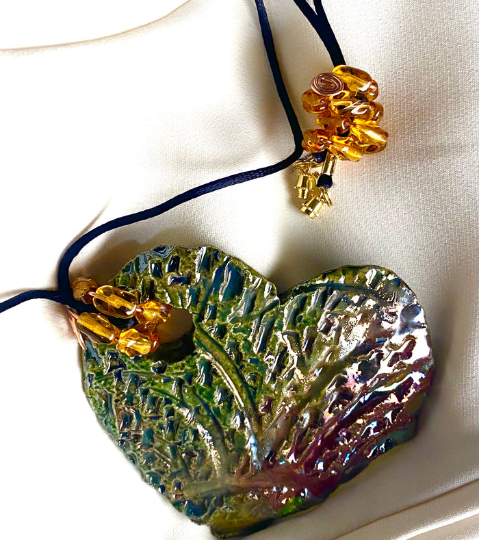 Have A Heart ! Each heart pendant is handmade with love! It is 3"x 3" and weighs approx. 3ozs. This pendant has an alligator green and gold metallic raku glazes that renders a unique translucent  patina. The heart  has a textured  pattern. It holds a spiral of amber mini beads on a spiral copper wire. This pendant has a nice 12" black suede cord!