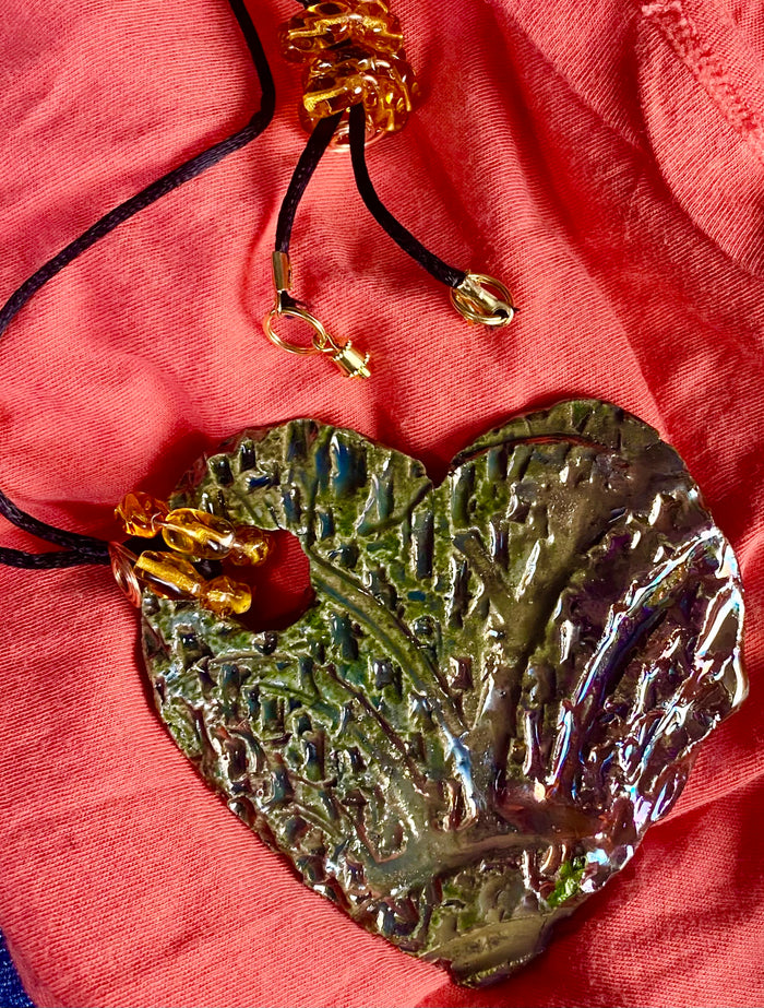 Have A Heart ! Each heart pendant is handmade with love! It is 3"x 3" and weighs approx. 3ozs. This pendant has an alligator green and gold metallic raku glazes that renders a unique translucent  patina. The heart  has a textured  pattern. It holds a spiral of amber mini beads on a spiral copper wire. This pendant has a nice 12" black suede cord!