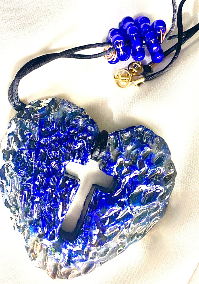Have A Heart ! Each heart pendant is handmade with love! It is 3"x 3" and weighs approx. 3ozs. This pendant has a royal blue and gold metallic raku glazes that renders a unique translucent  patina. The heart has a cut out cross in the center with a textured  pattern. It holds a spiral of royal blue mini beads on a spiral copper wire. This pendant has a nice 12" black suede cord!