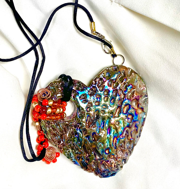 Have A Heart ! Each heart pendant is handmade with love! It is 3"x 3" and weighs approx. 3ozs. This pendant has a copper gold metallic raku glazes that renders a unique translucent  patina. The heart has a textured pattern . It holds a spiral of amber and red mini beads on a spiral copper wire. This pendant has a nice 12" black suede cord!