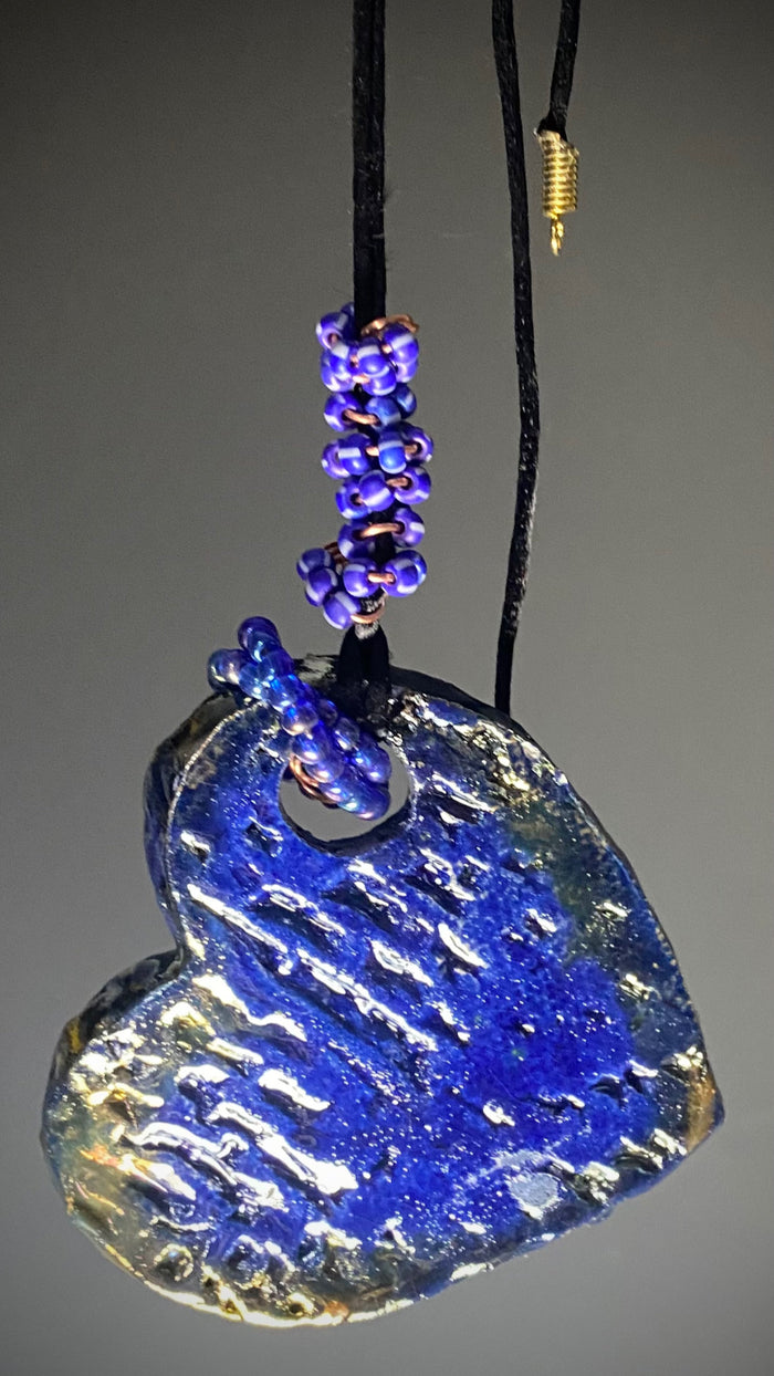 Have A Heart! Each heart pendant is handmade with love! It is 3"x 3"and weighs approx. 3ozs. This pendant has a blue and gold raku glazes that renders a unique translucent  patina. The heart has a textured pattern! Both sides are  are different and equally beautiful! There is a spiral of blue mini beads on copper in the center. This pendant has a nice 12" black adjustable rattail cord!