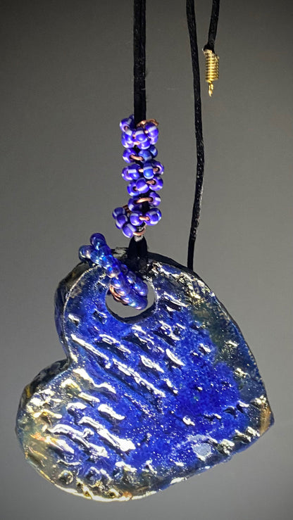 Have A Heart! Each heart pendant is handmade with love! It is 3"x 3"and weighs approx. 3ozs. This pendant has a blue and gold raku glazes that renders a unique translucent  patina. The heart has a textured pattern! Both sides are  are different and equally beautiful! There is a spiral of blue mini beads on copper in the center. This pendant has a nice 12" black adjustable rattail cord!