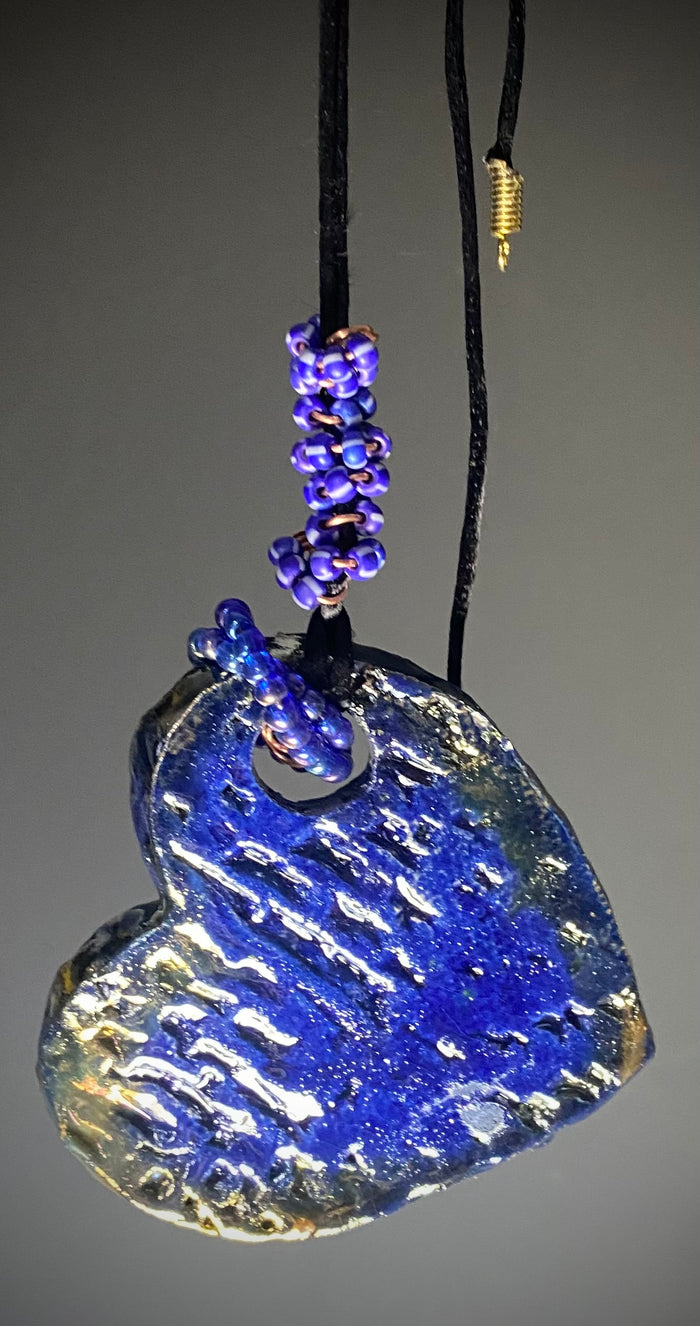 Have A Heart! Each heart pendant is handmade with love! It is 3"x 3"and weighs approx. 3ozs. This pendant has a blue and gold raku glazes that renders a unique translucent  patina. The heart has a textured pattern! Both sides are  are different and equally beautiful! There is a spiral of blue mini beads on copper in the center. This pendant has a nice 12" black adjustable rattail cord!